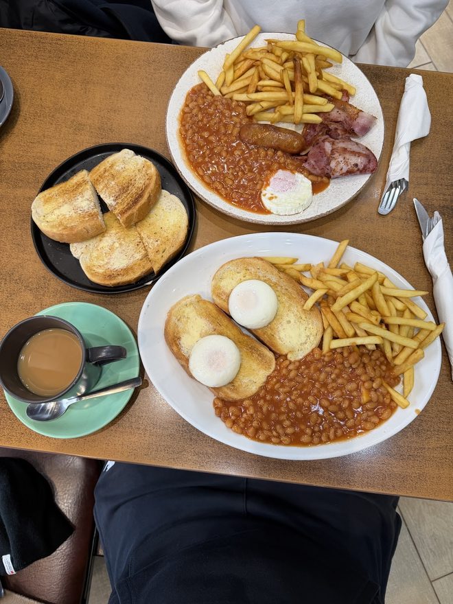 Two breakfast plates with beans, chips, eggs, sausage, bacon and toast on a wooden table