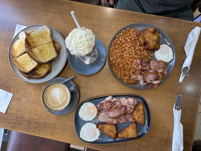 A table from above with two breakfast plates, toast, a milkshake and two lattes