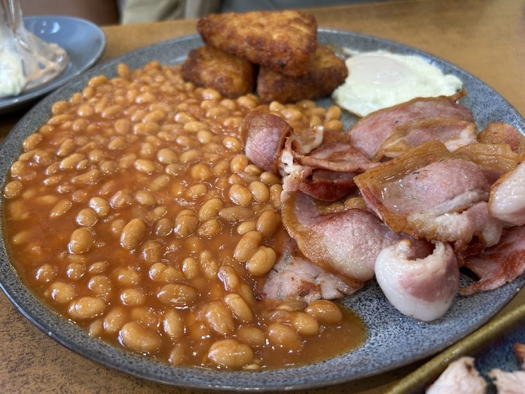 A plate of baked beans, bacon rashers, hash browns and a fried egg